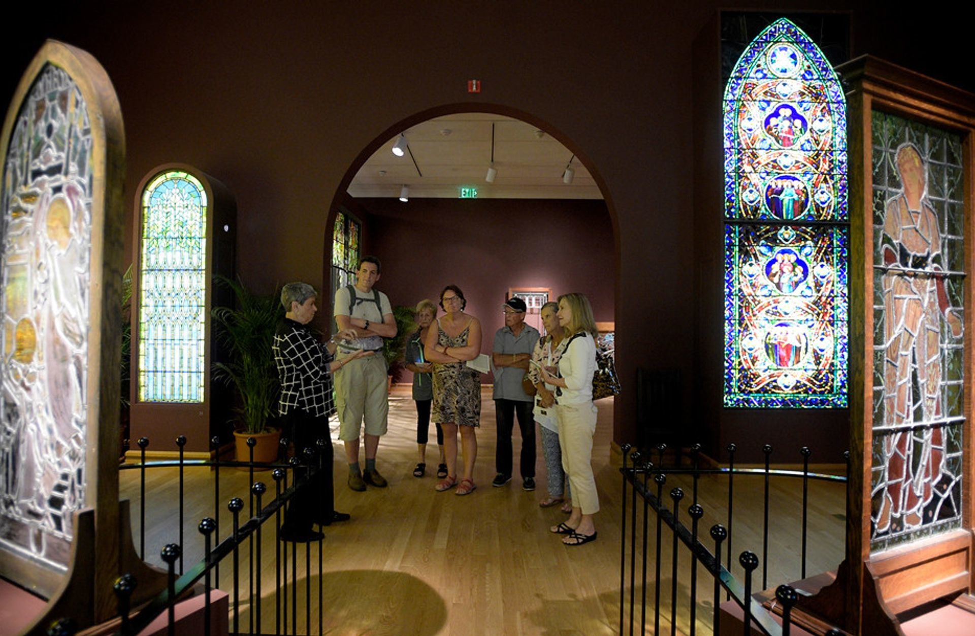 people walking into an exhibit with stained glass windows and black metal fence